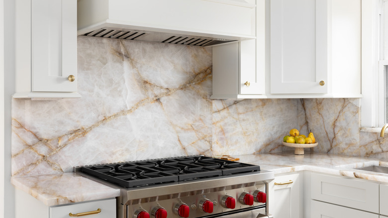 White marble with gold veins being used as a kitchen backsplash in a white kitchen