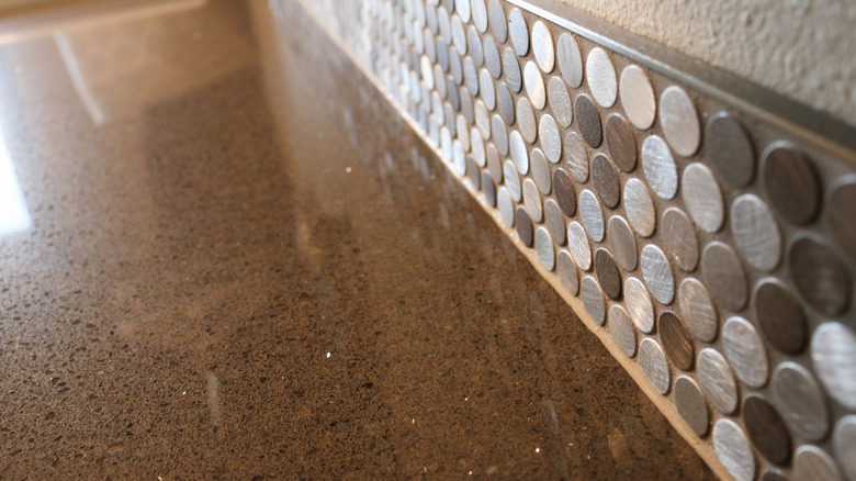 A metal edge is installed above a penny tile backsplash and glossy stone-look laminate countertop