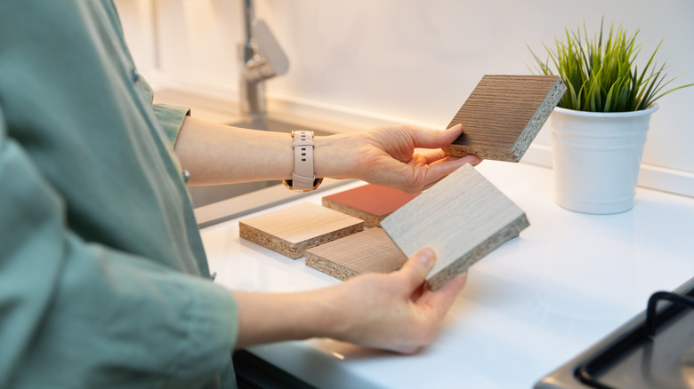 A woman holds two laminate countertop samples in a kitchen
