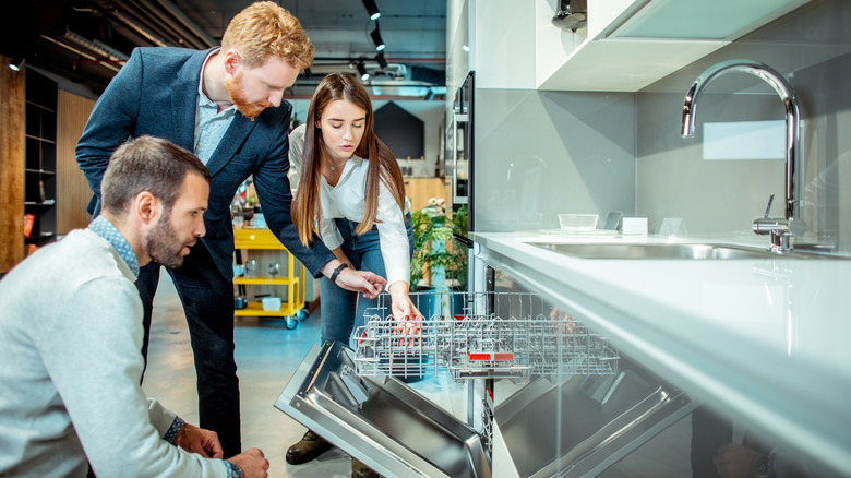 A salesman helps a young couple look at a dishwasher in a retail store.