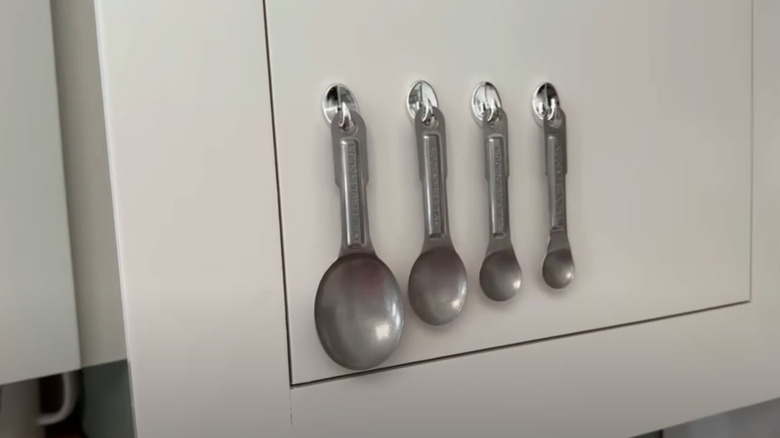 Metal measuring spoons hung on hooks affix to a cabinet door.