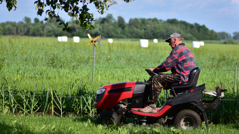 A man using a riding lawn mower to cut tall grass
