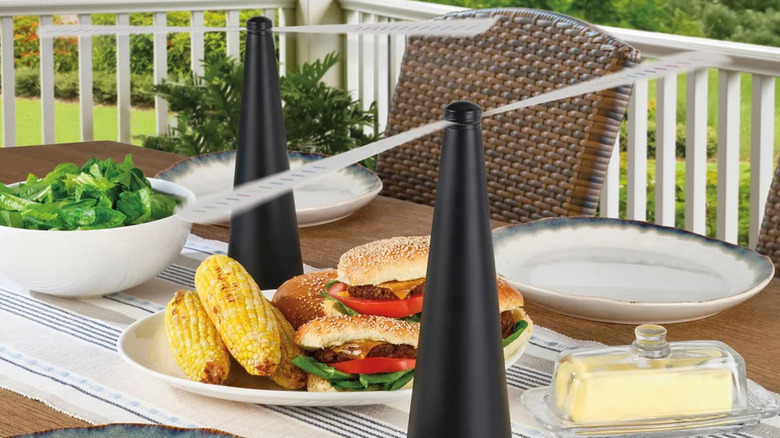 Two black bug repelling fans sit on a patio table laden with food