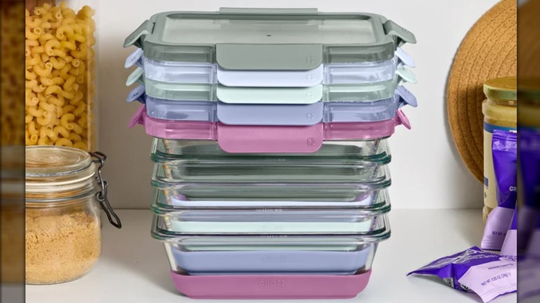 Glass meal prep containers with colorful lids are stacked on a white kitchen counter