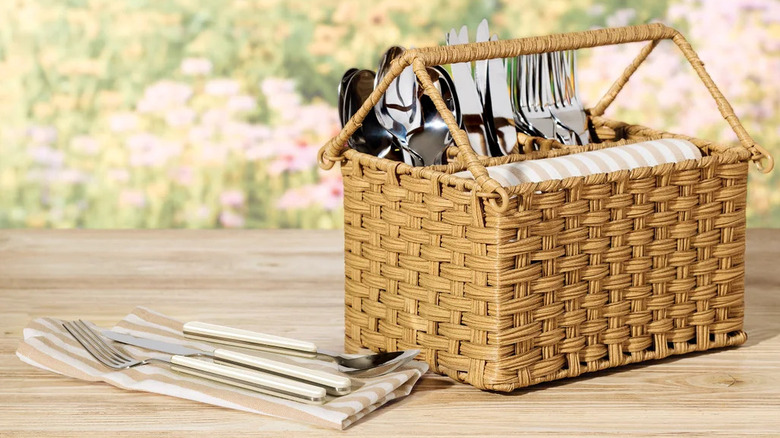 A woven basket caddy is full of silverware and striped napkins