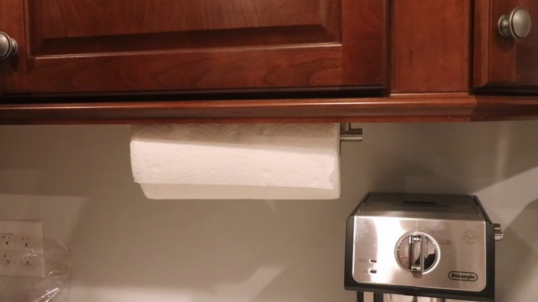 Paper towel hanging on metal rod mounted beneath red wood kitchen cabinets