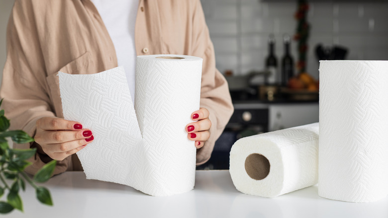 person tearing a paper towel in a kitchen with two unused ones lying on the counter