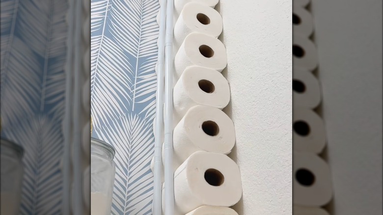 Paper towels stacked in back closet against wall behind two white tension rods