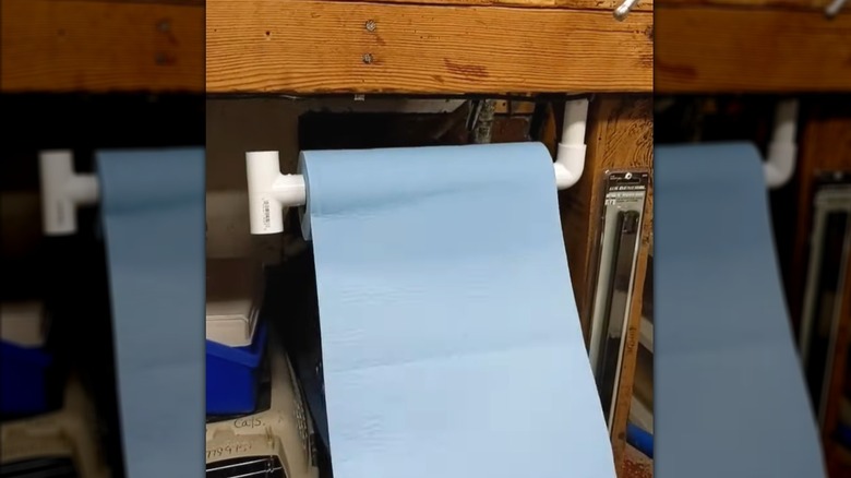 Blue paper towel hanging on homemade PVC pipe holder beneath wooden work table