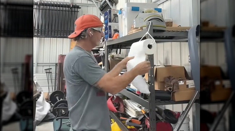 Man unrolling paper towel from DIY hanger in messy home garage