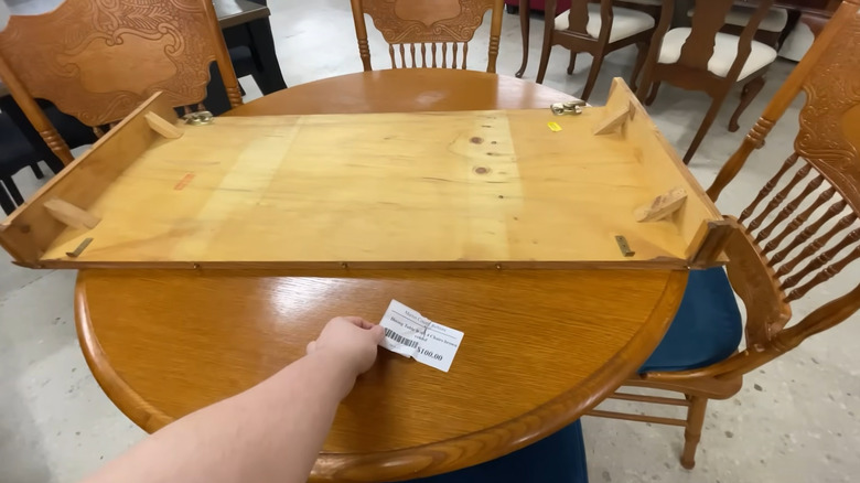 Person shopping for furniture in a thrift store reaching for the tag on a dining table