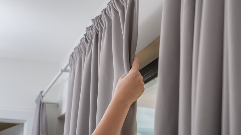 A hand pulls a gray curtain closed