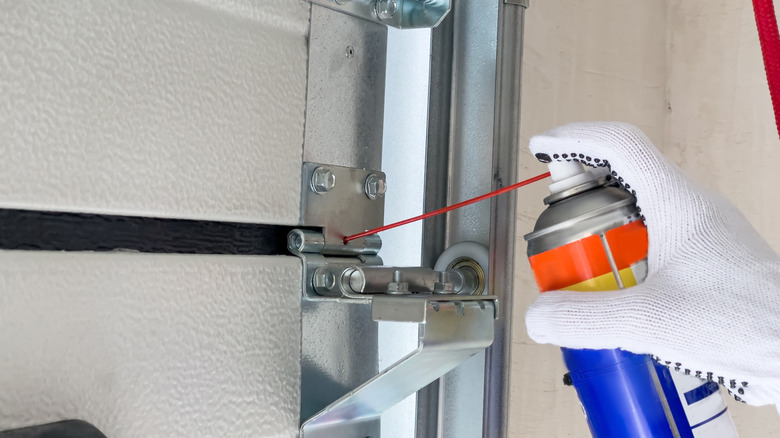 Worker wearing gloves and lubricating garage door