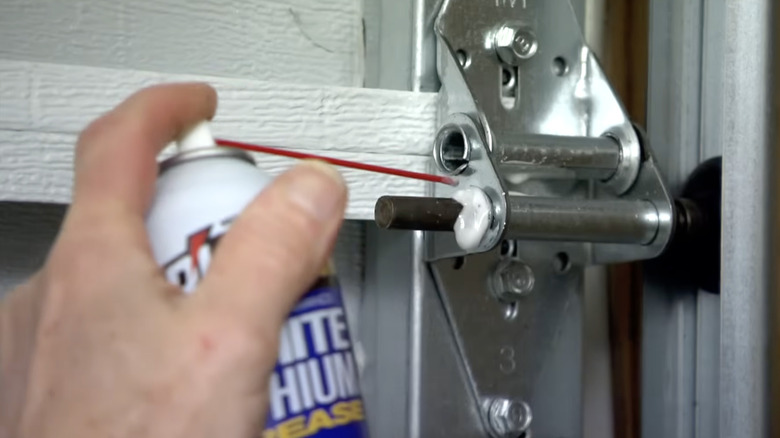 Homeowner using lubricant on garage door hinge