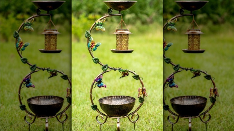 A solar light glowing on the middle tier of a bird feeder, hanging from a metal chain and framed by a decorative screen.