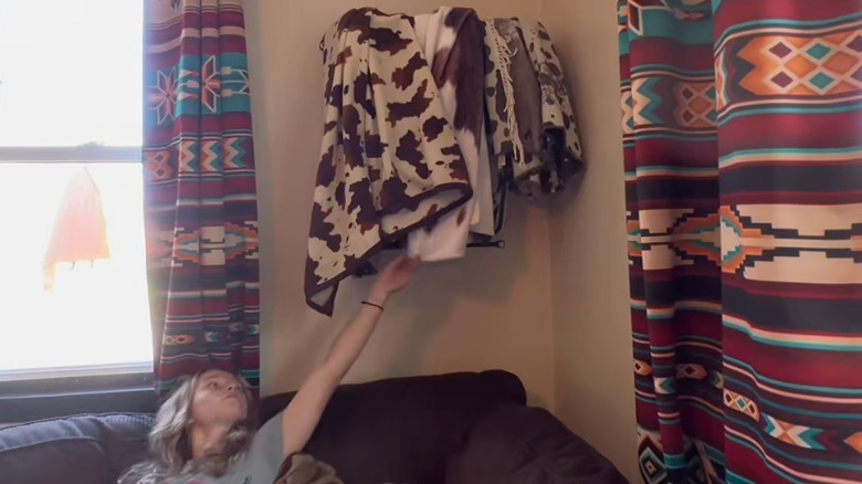 Woman pulling a blanket down from a hay rack on the wall used for blanket storage