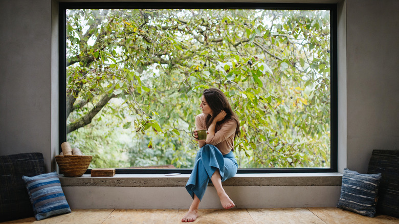 Woman drinking tea before a large window