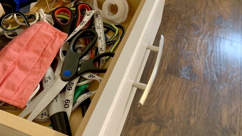 A junk drawer is opened to reveal a jumble of scissors, tape, masks, and random items