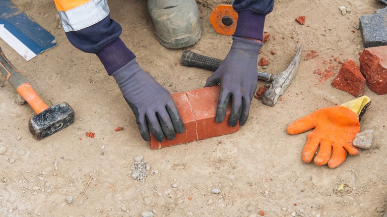 A worker wearing rubber gloves separating a brick with a brick hammer