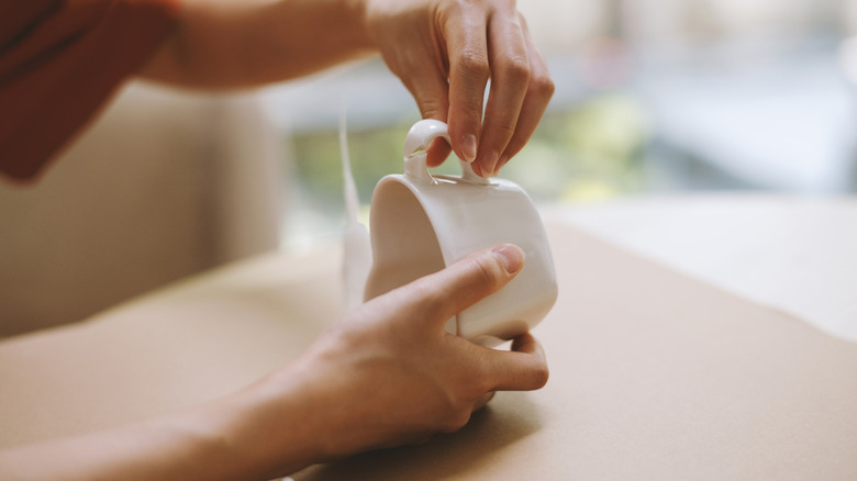 Person holding a white heart-shaped mug that has the handle broken off