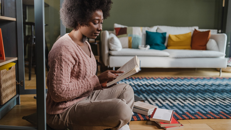 A woman reads a book on the floor, with a collection of books by her