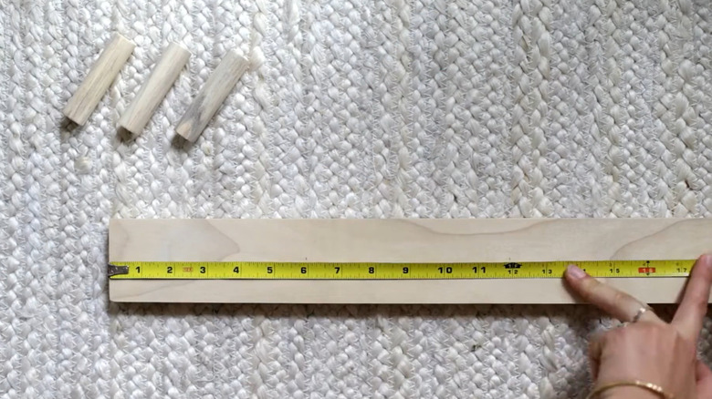 A woman measuring a wood board with wooden pegs nearby