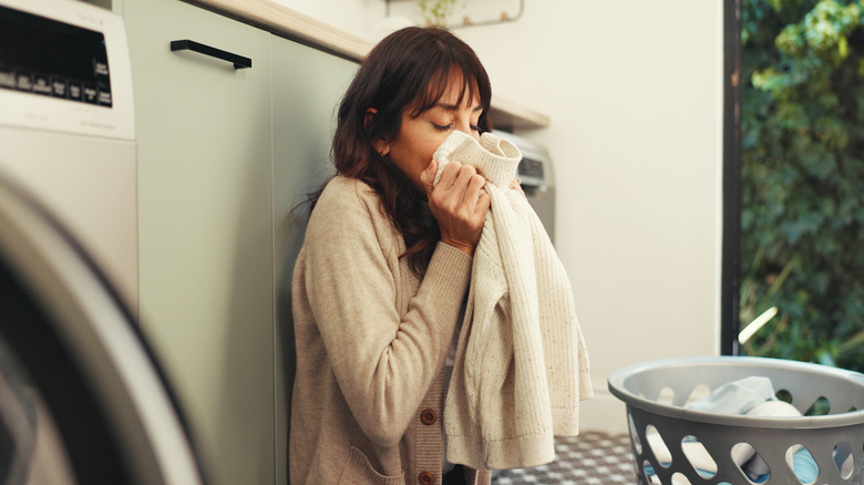 Woman sitting on the ground with her eyes closed while smelling a sweater fresh from the laundry