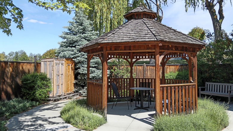 A wooden gazebo sits in a large backyard
