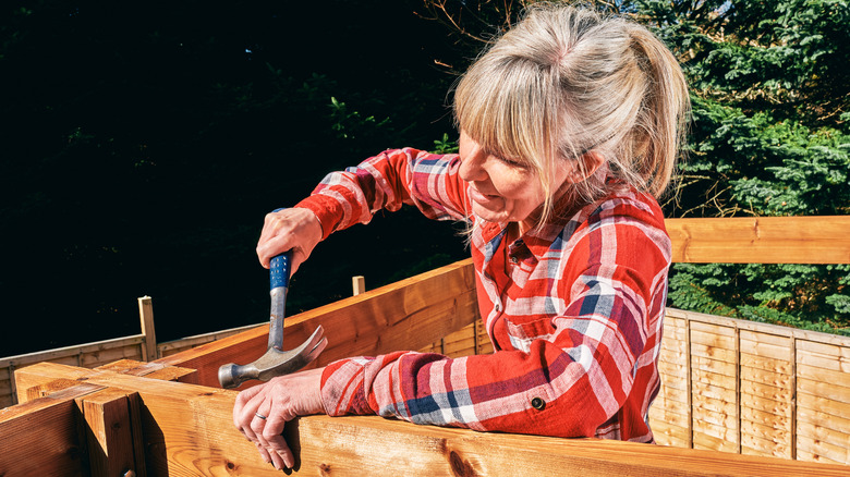 A woman uses a hammer to assemble a backyard gazebo
