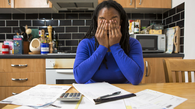A woman surrounded by bills holds her head in her hands