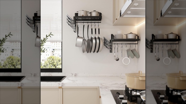 The X-cosrack pot racks full of pots, pans, and kitchen utensils hanging on a white kitchen wall.