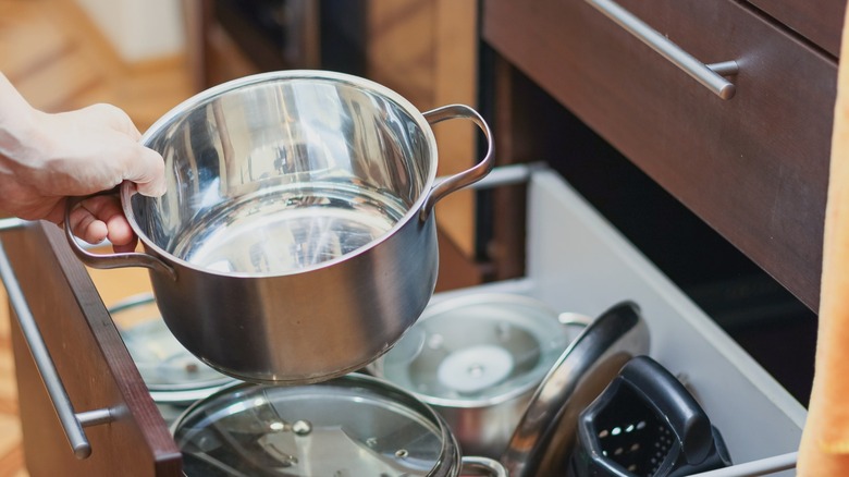 Person putting a pot away in a crowded kitchen drawer