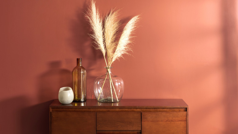 Decorative glass jars sit on a wooden table in front of a wall painted a terra cotta color
