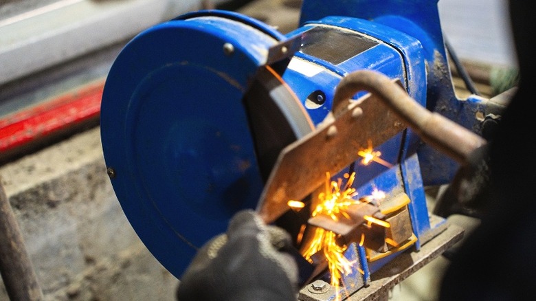 Person grinding rust off of a rusty garden hoe with a bench grinder