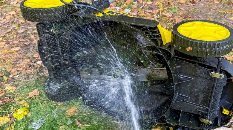 Lawn mower tipped on its side being washed with a garden hose