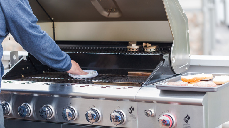 Man wiping down an outdoor gas grill with a cloth