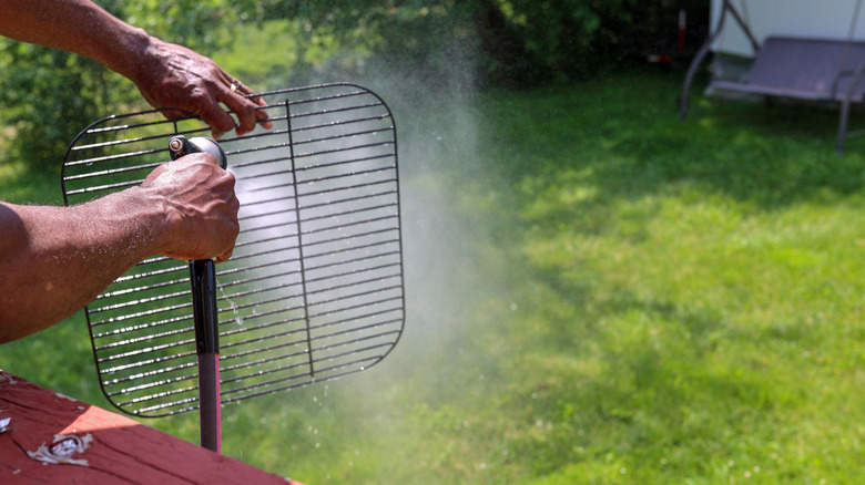 A man hosing down a cooking grate outside