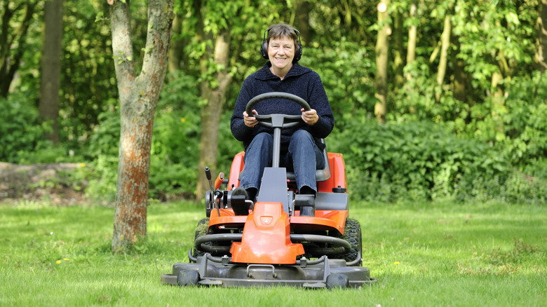 Woman on riding lawn mower wearing ear protection