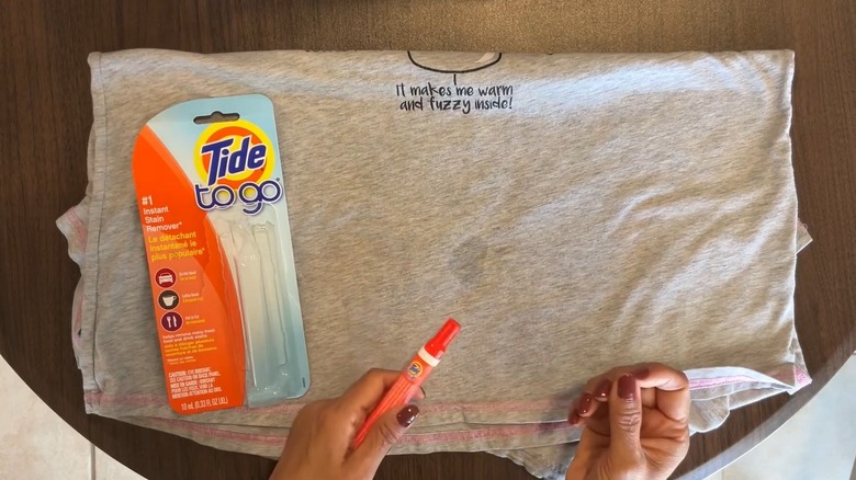 Person holding Tide pen over a shirt with a stain