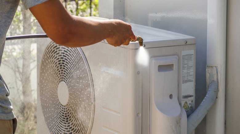 A person spraying an outdoor AC unit with a water hose