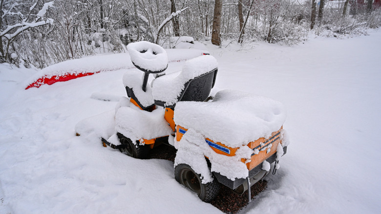 A riding lawn mower covered in snow outside