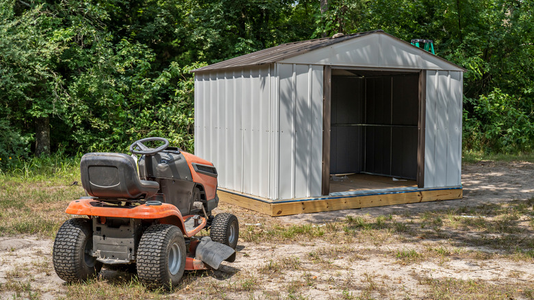 Riding lawn mower outside of a metal shed