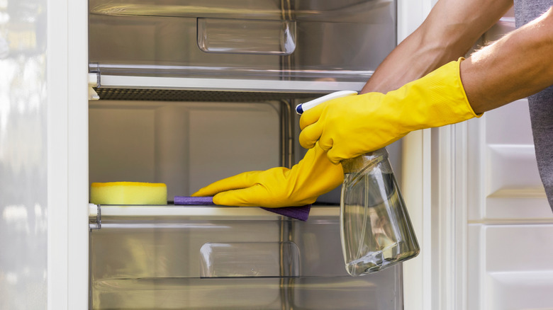 Person wearing yellow rubber gloves cleaning an empty fridge.