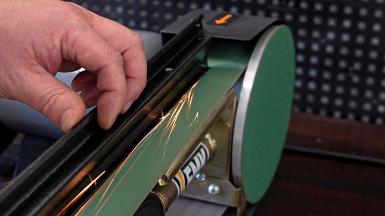 Person sanding metal on a bench grinder converted to be a belt sander