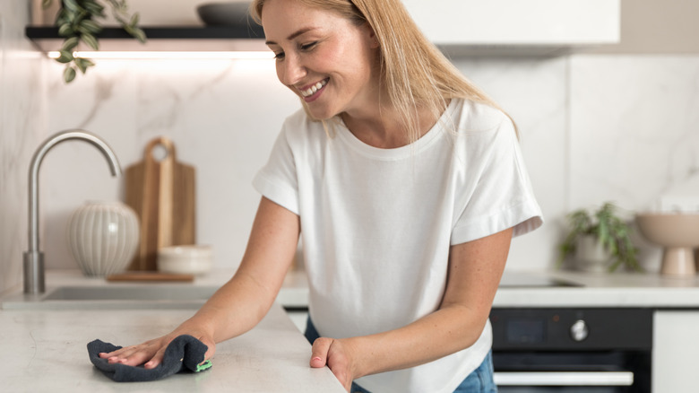A woman cleaning a quartz countertop with a microfiber cloth.