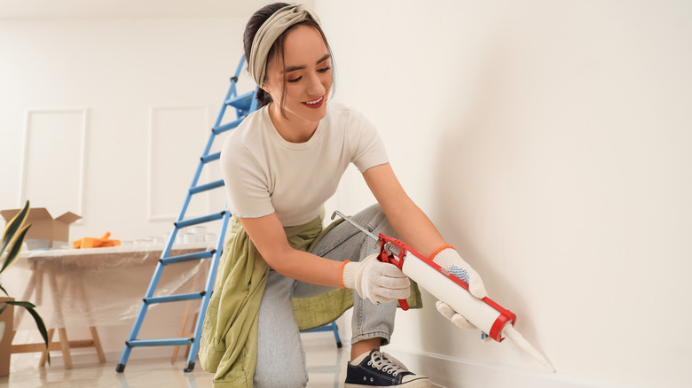 A woman sealing a baseboard with caulk.