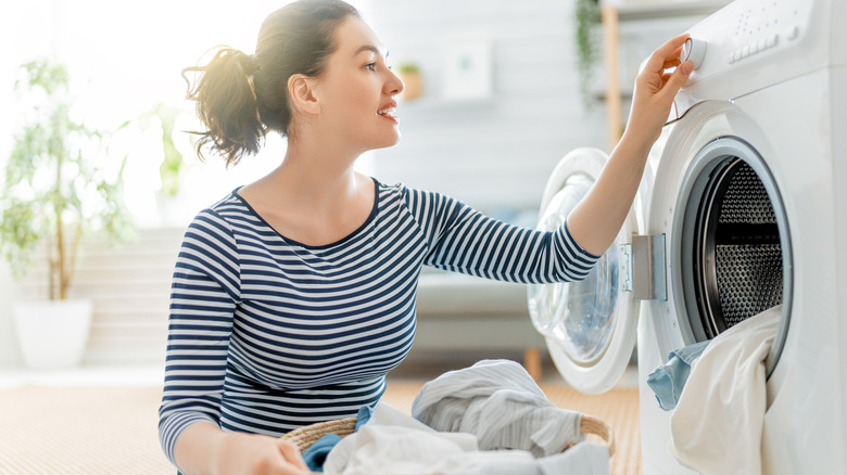 A woman loads light clothes into a washing machine