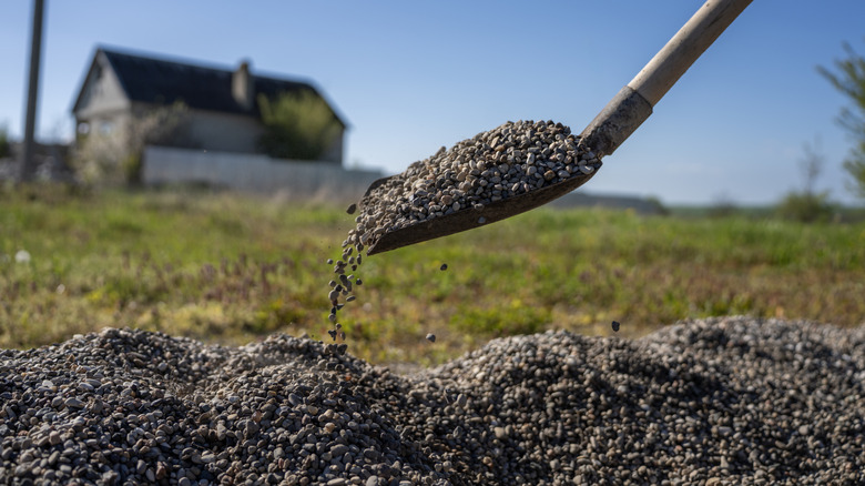 A shovel pouring small dark gray gravel into a pile