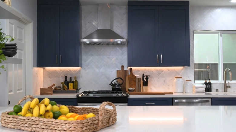 Kitchen featuring navy cabinetry and white marble herringbone backsplash.