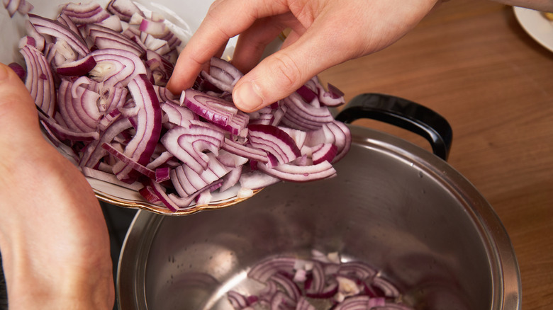 hand putting cut red onions into pan